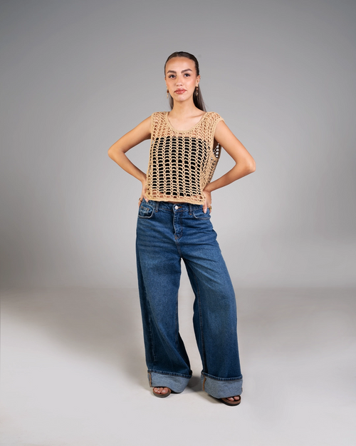 Woman wearing a brown crochet top and blue jeans on a gray background