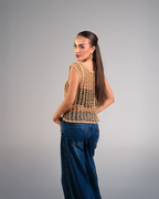 Woman wearing a beige crochet top and blue jeans on a gray background