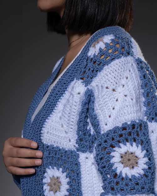 Close-up of a person wearing a blue and white crocheted cardigan with floral patterns.