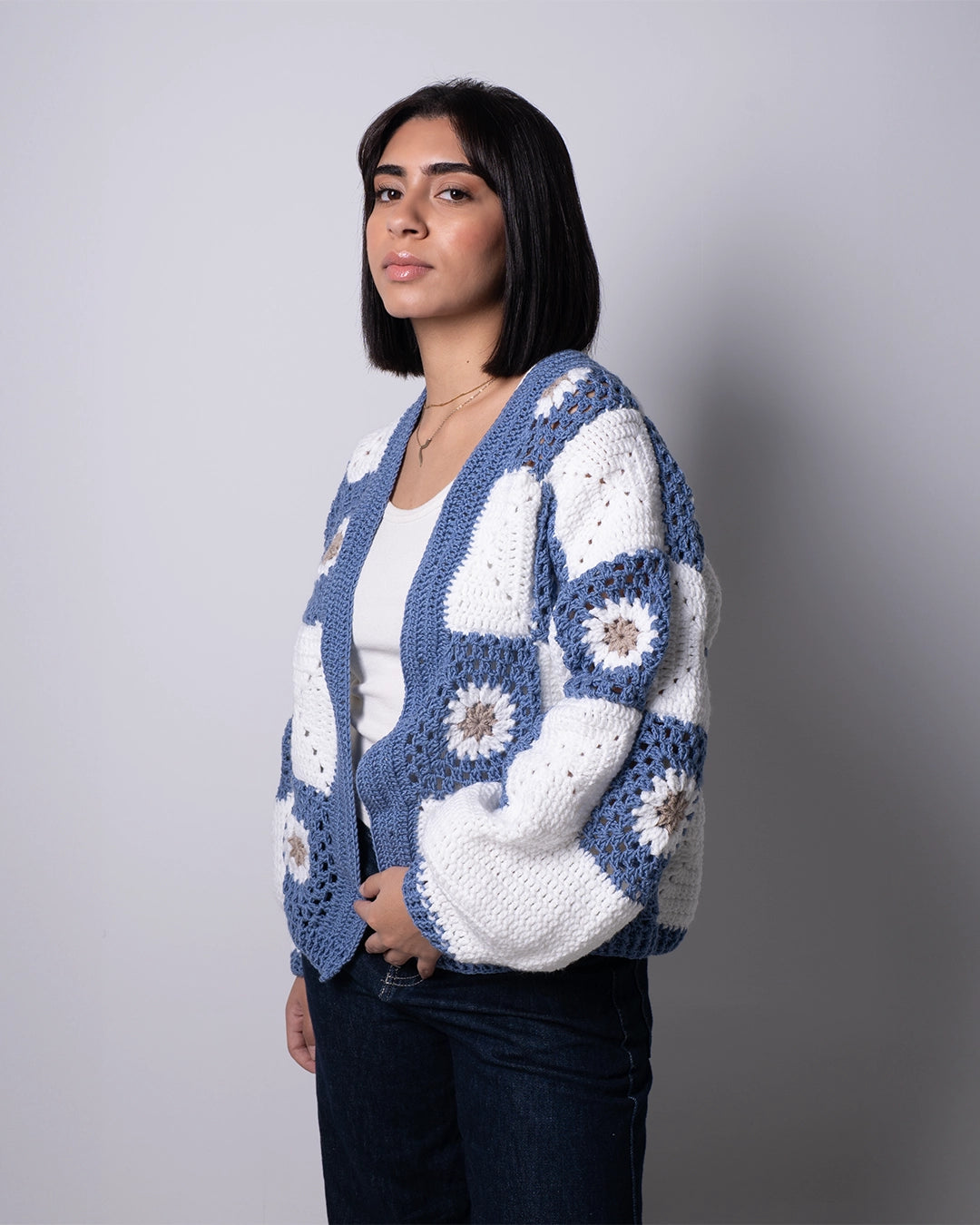 Woman wearing a blue and white crochet cardigan against a gray background