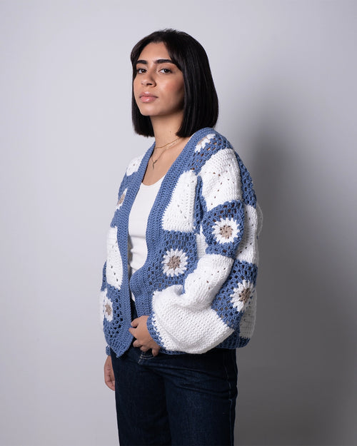 Woman wearing a blue and white crochet cardigan against a gray background