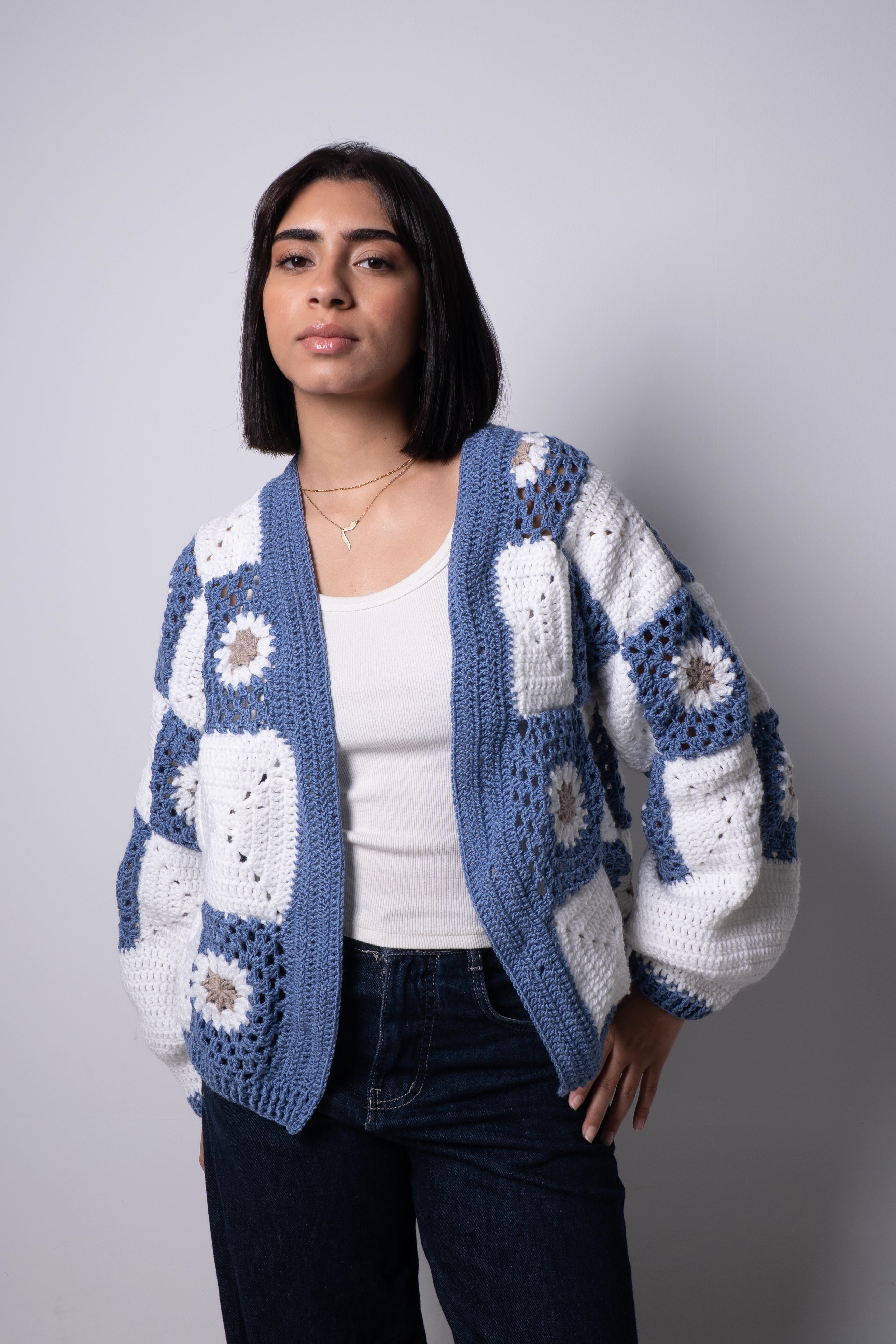 Woman wearing a blue and white crocheted cardigan against a plain background