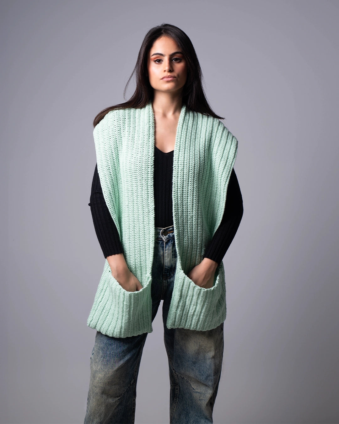 Woman wearing a light green knitted vest against a gray background