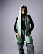 Person wearing a light green knitted scarf with a hood on a gray background