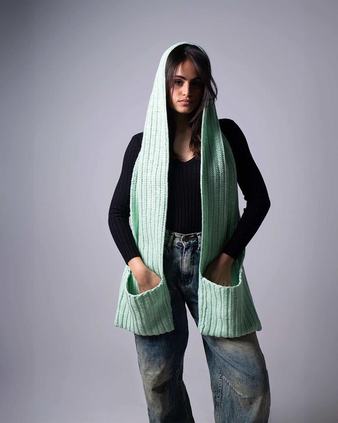 Person wearing a light green knitted scarf with a hood on a gray background