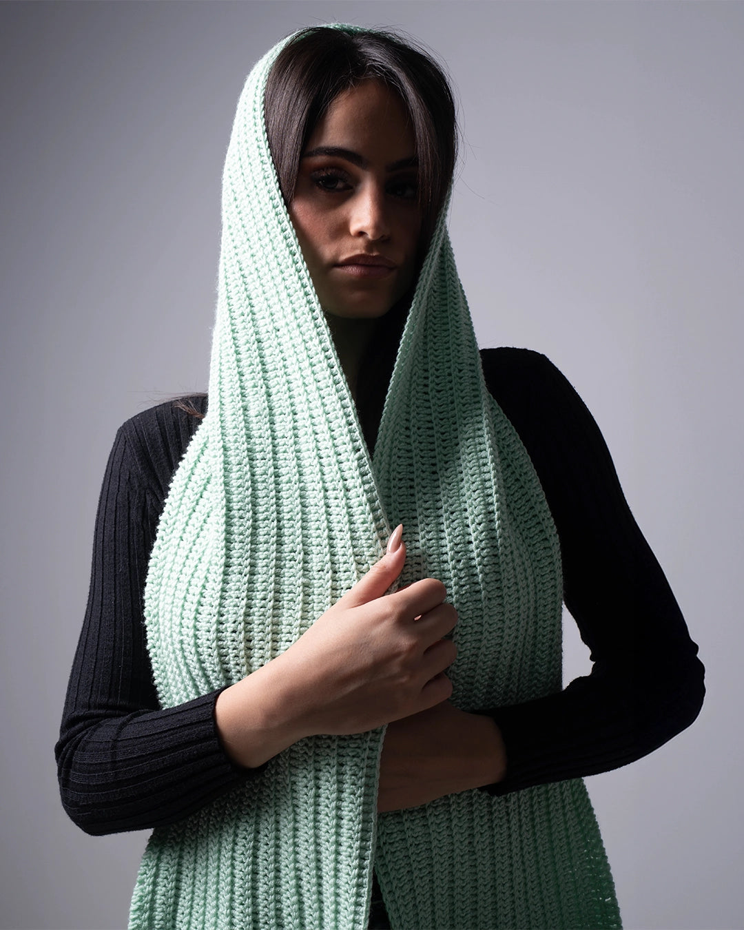Woman wearing a long green knitted scarf against a gray background