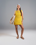 Woman wearing a yellow patterned dress holding a beige bag on a gray background