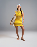 Woman wearing a yellow patterned dress holding a beige bag on a gray background