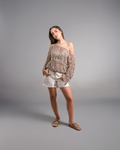 Woman wearing a patterned off-shoulder top and white shorts on a gray background