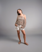 Woman wearing a patterned off-shoulder top and white shorts on a gray background