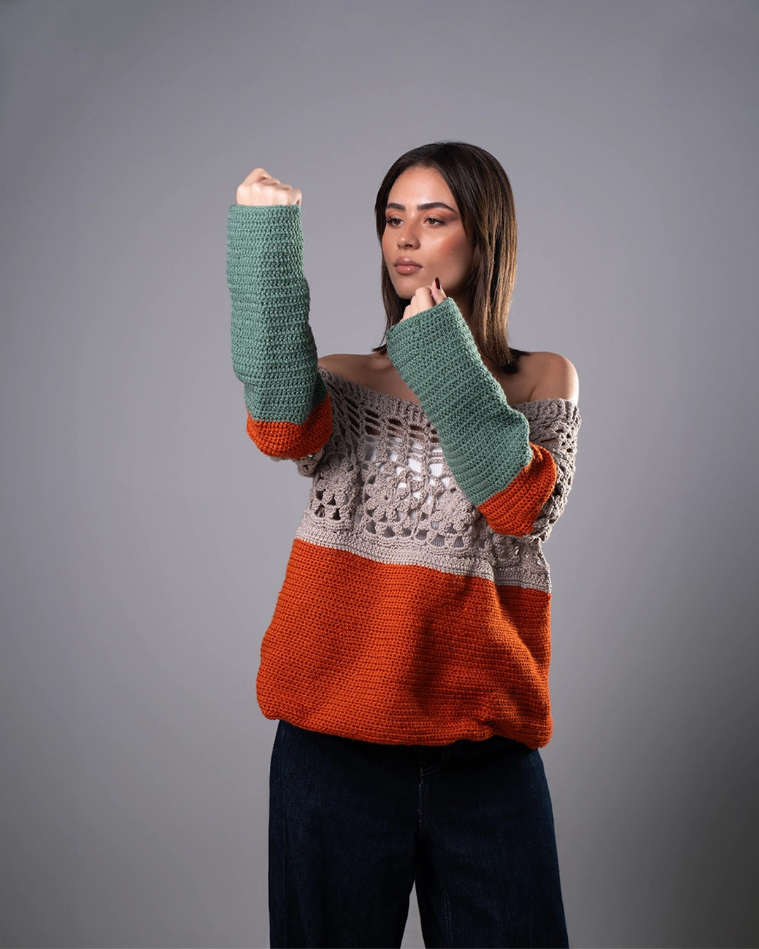 Woman wearing a colorful sweater with green sleeves and orange bottom half on a gray background