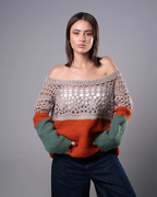 Woman wearing a crocheted sweater with color-blocked design on a gray background