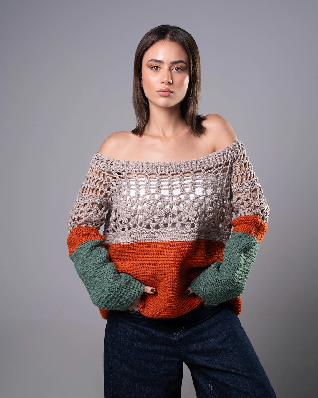 Woman wearing a crocheted sweater with color-blocked design on a gray background