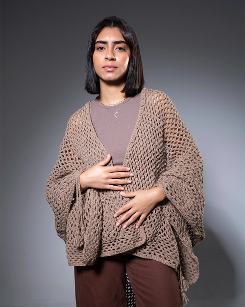 Woman wearing a brown knitted poncho against a gray background