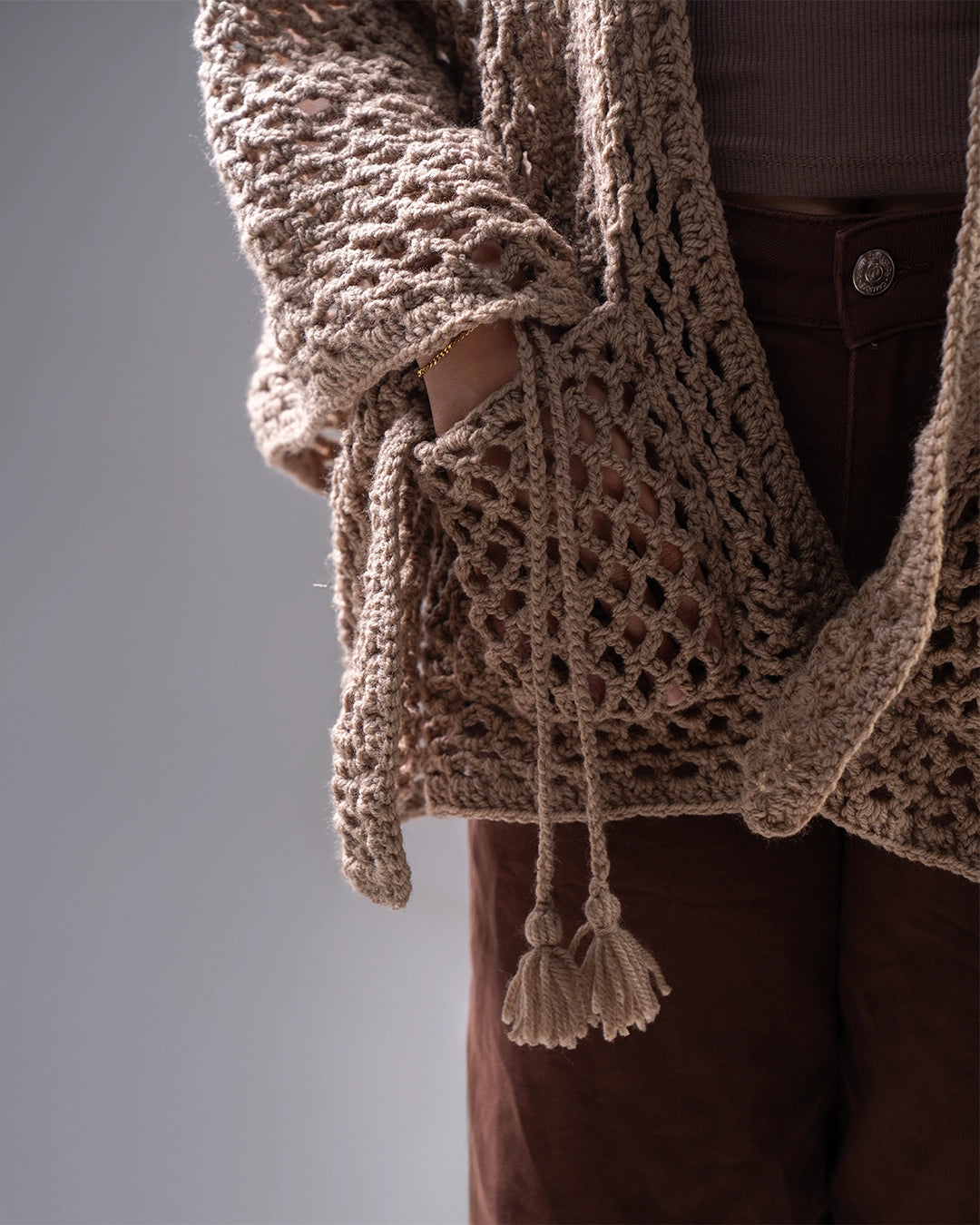 Close-up of a brown knitted cardigan with tassels on a neutral background