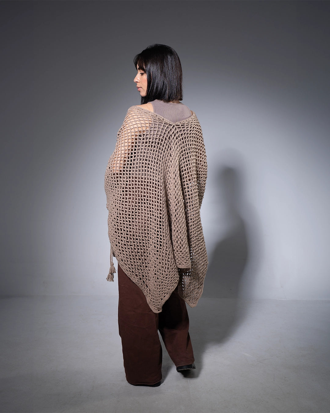 Woman wearing a brown knitted poncho against a gray background