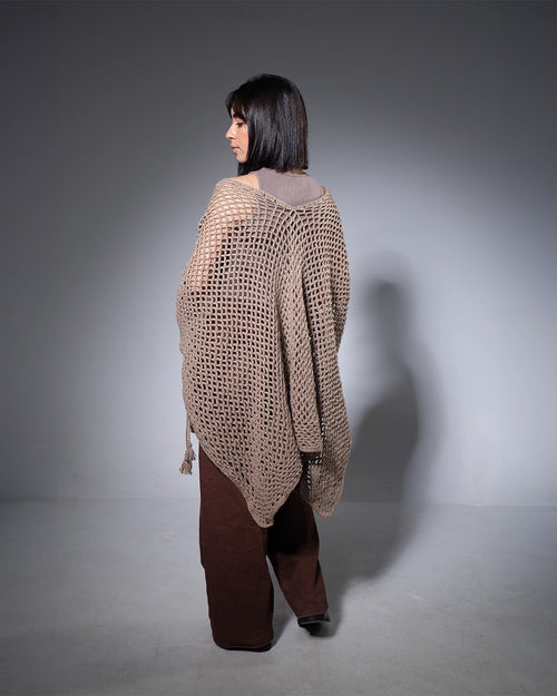 Woman wearing a brown knitted poncho against a gray background
