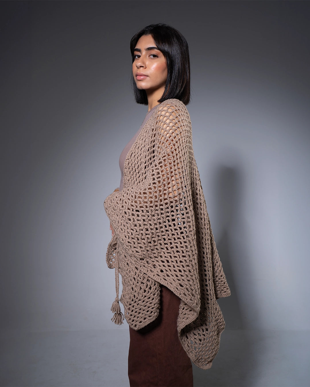 Woman wearing a beige knitted poncho against a gray background