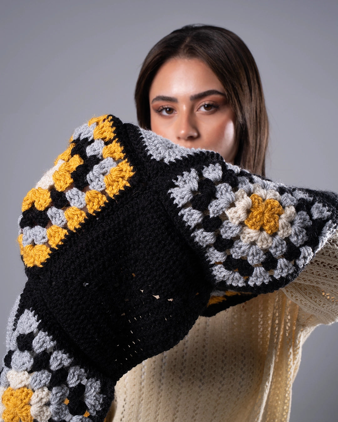 Woman holding a colorful crocheted blanket with a gray background