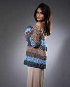 Woman wearing a crocheted sweater with blue and brown pattern on a gray background