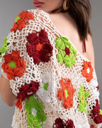 Woman wearing a crochet top with red, orange, and green floral patterns on a gray background