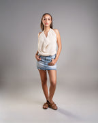 Woman wearing a white sleeveless top and denim shorts on a gray background