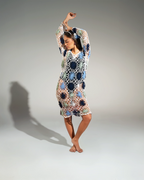 Woman wearing a colorful crochet dress against a plain background