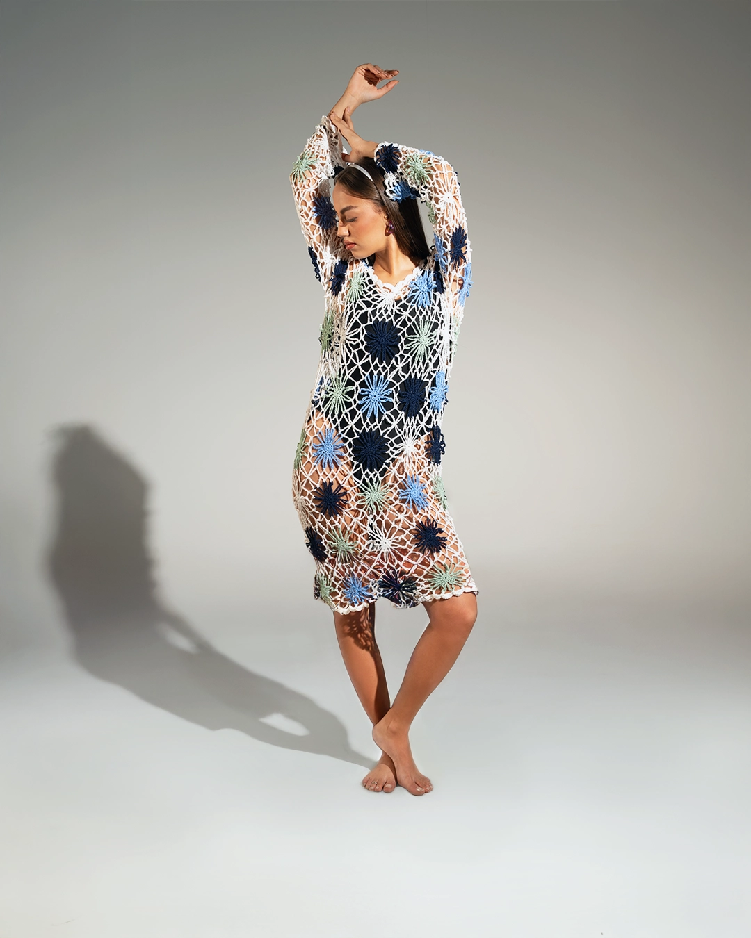 Woman wearing a colorful crochet dress against a plain background
