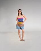 Woman wearing a colorful striped top and denim shorts on a gray background