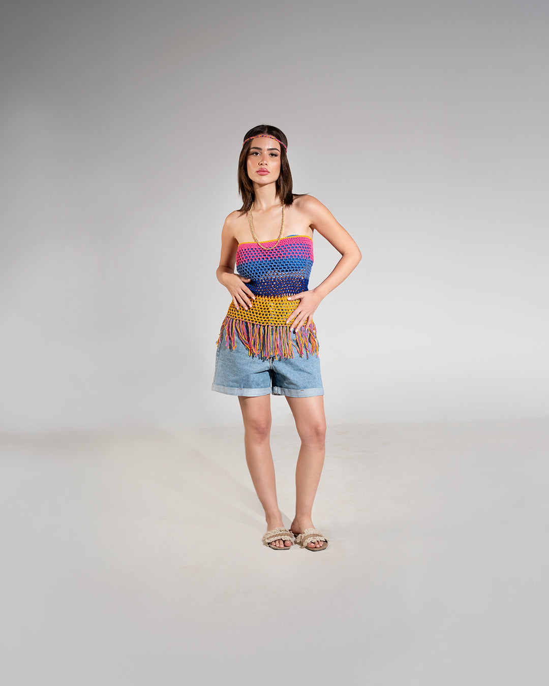Woman wearing a colorful striped top and denim shorts on a gray background