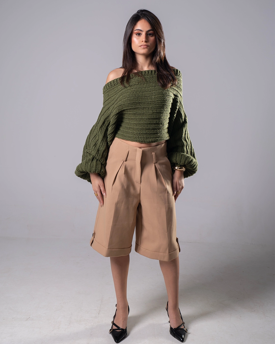 Woman wearing a green knitted sweater and beige shorts on a gray background