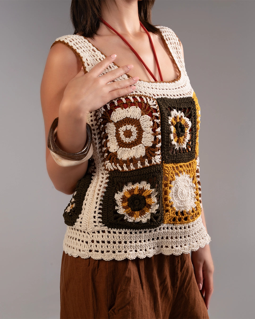 Person wearing a crocheted square-patterned top with brown and beige colors on a gray background