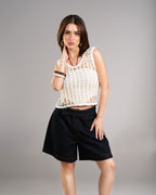 Woman wearing a white crochet top and black shorts on a gray background