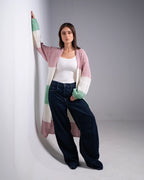 Woman wearing a long, colorful cardigan over a white top and dark pants on a plain background