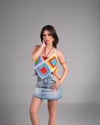 Woman wearing a colorful crochet top and denim skirt on a gray background