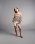 Woman wearing a patterned off-shoulder top and white shorts on a gray background
