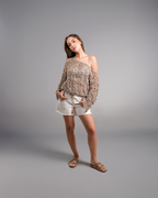 Woman wearing a patterned off-shoulder top and white shorts on a gray background