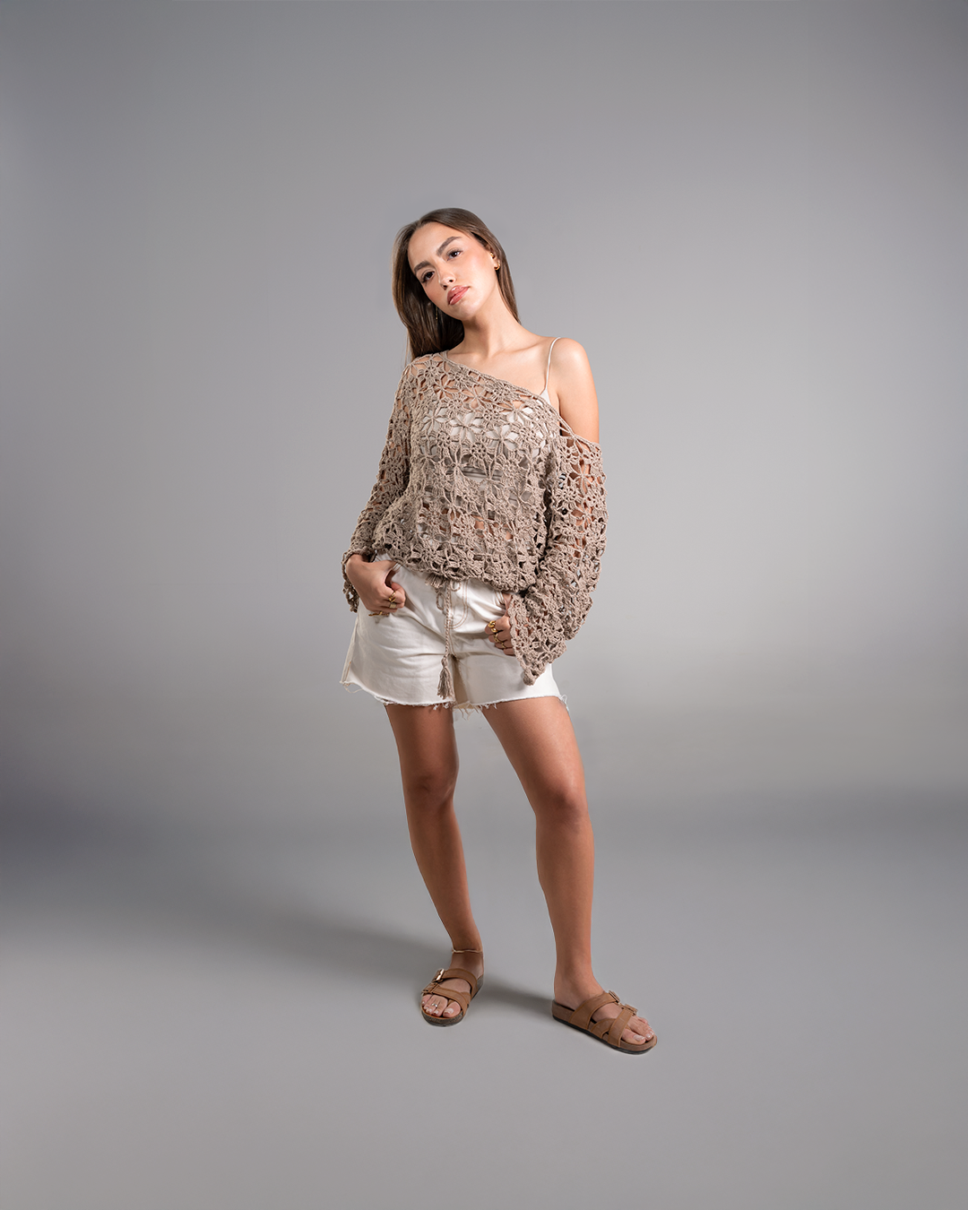 Woman wearing a patterned off-shoulder top and white shorts on a gray background